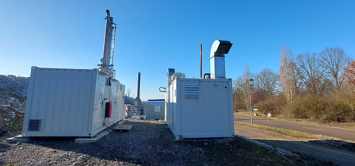 Zwei technische Containeranlagen mit Abluftsystemen stehen nebeneinander auf einem geschotterten Gelände. Es handelt sich um eine Schwachgasverbrennungsanlage der AWRM.