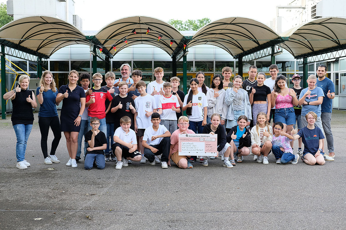 Gruppenfoto bei der Preisverleihung des Schulwettbewebs zur Kreisputzete, zwei Schüler halten einen großen symbolischen Scheck, alle zeigen Daumen hoch und lächeln.