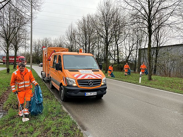 Oranges Fahrzeug der Straßenmeisterei, Mitarbeiter im Vordergrund beim Müllsammeln