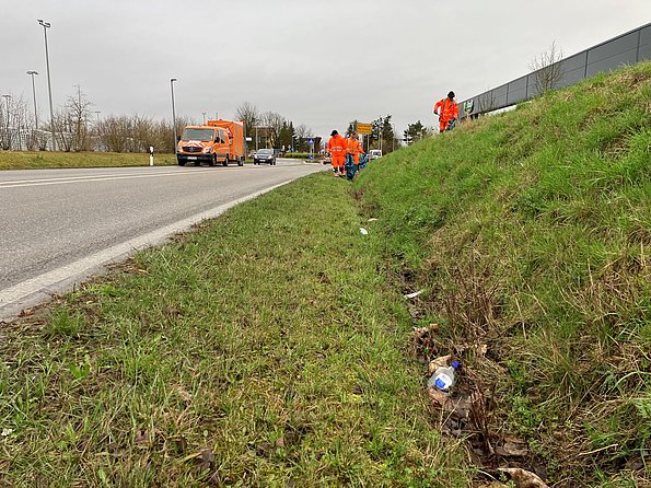  Mitarbeiter in orangener Kleidung beim Müllsammeln am Straßenrand