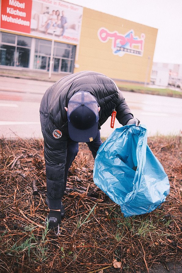 Person beim Müllsammeln mit blauem Müllsack
