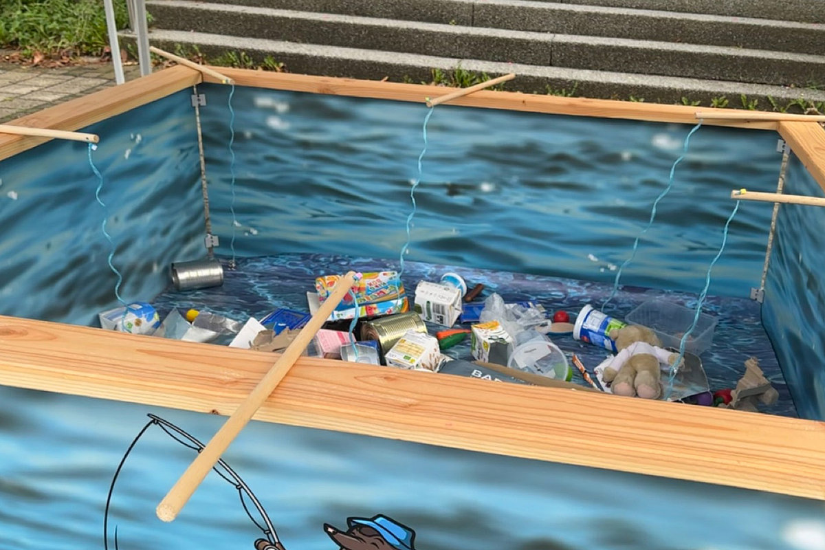 Becken mit Wasseroptik und verschiedenen Müllgegenständen wie Dosen, Verpackungen, Schuhen und Spielzeug – Teil eines Angelspiels.