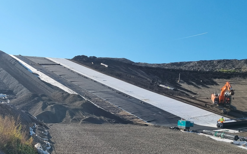 Fläche auf der Deponie mit Kies und Abdeckplanen vor blauem Himmel