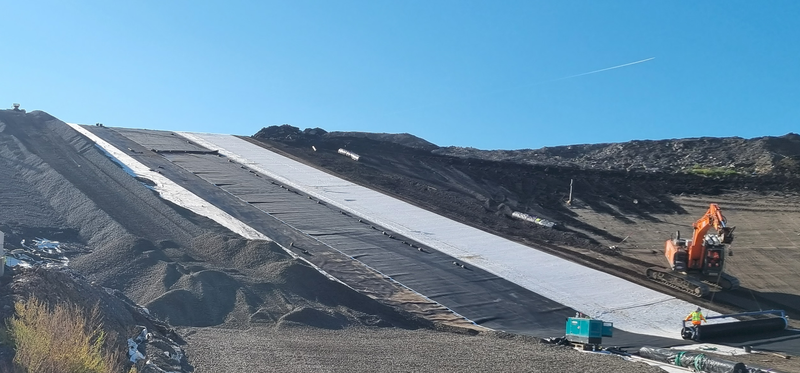 Fläche auf der Deponie mit Kies und Abdeckplanen vor blauem Himmel