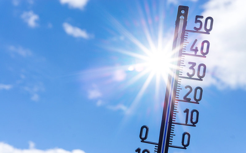 Blauer Himmel mit Sonne und Wolken, davor ein Thermometer