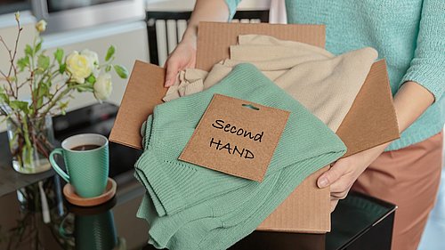 Kleidungsstücke im Karton mit Hinweis Second Hand